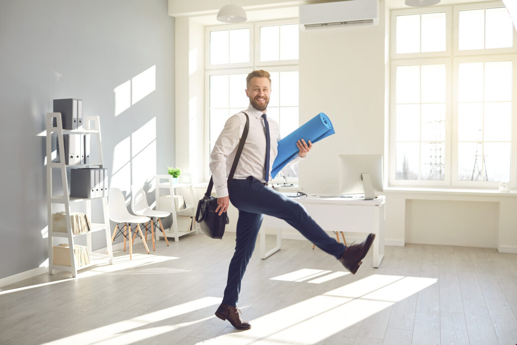 Funny businessman with a beard with a yoga mat goes for a workout in the office. The end of the working day at the office. Workplace health meditation. Active lifestyle.
